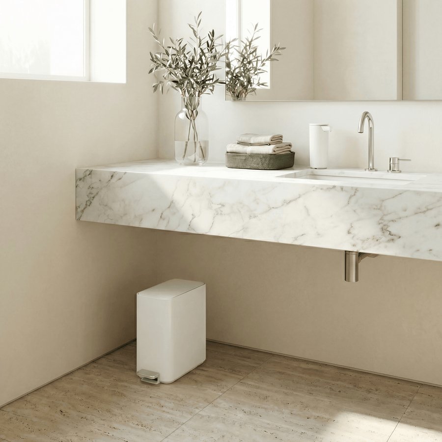 Simplehuman's 9L Slim Step Can in White in a very bright bathroom environment with white marble sink counter top and walls featuring a Simplehuman Sensor Pump in white on the countertop.