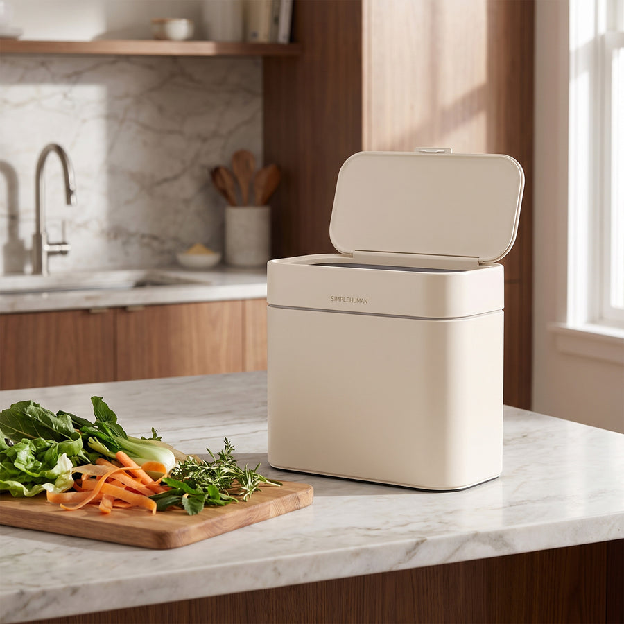 Simplehuman's Compost Caddy in a Latte finish on a modern kitchen countertop made of marble. 