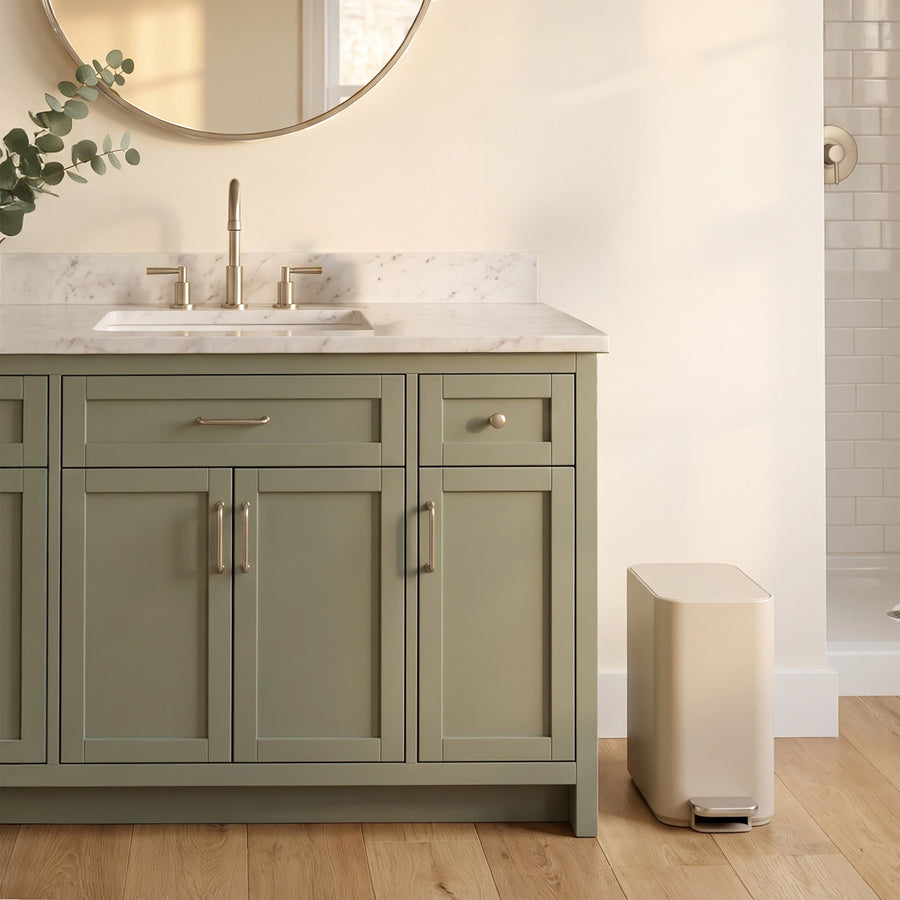 Simplehuman's 5L Slim Step Can in Latte in a modern bathroom setting with green cabinetry and marble countertops. 