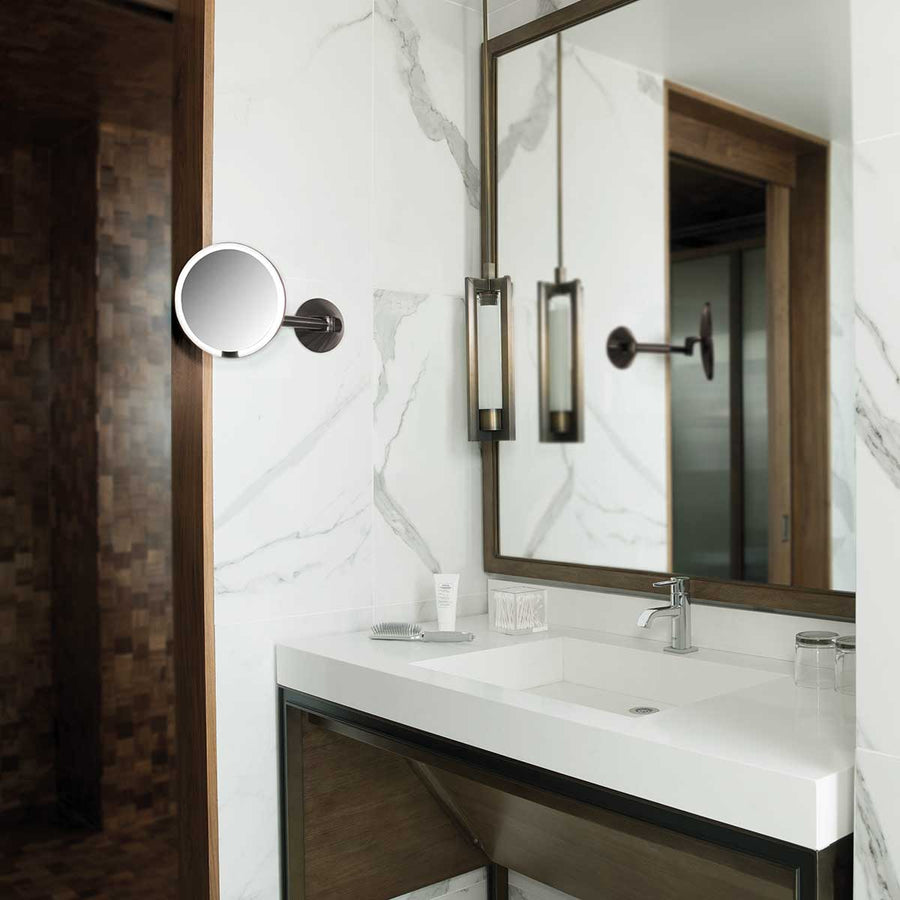 Lifestyle view of Simplehuman Dark Bronze Wall Mount Sensor Mirror in luxury bathroom, rechargeable, adjustable arm.